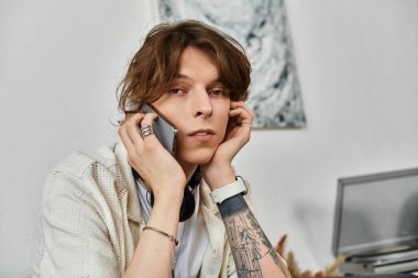 Genç bir adam evde dinlenirken telefonuyla konuşuyor. Etrafı çalışma malzemeleriyle çevrili..