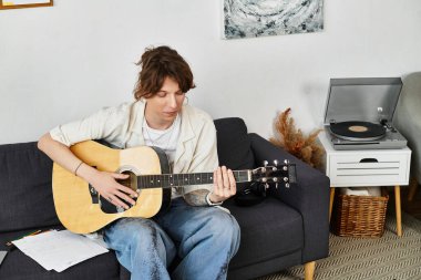 Adam, kişisel dokunuşlarla dolu rahat bir evde gitar çalmaya odaklanıyor..