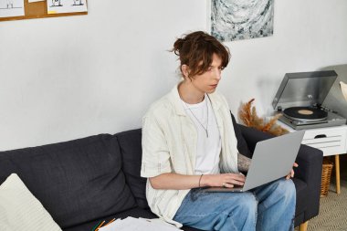 Odaklanmış genç bir adam, etrafı dekorla çevriliyken evinin konforundan laptopuyla çalışır..