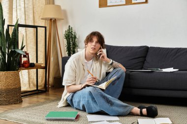 Adam evde oturmuş, etrafındaki çalışma materyalleriyle telefonda notlar alıyor..