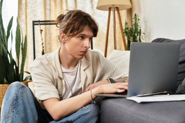 Evde derslere dalmış, rahat bir yerden dizüstü bilgisayarla çalışıyor..