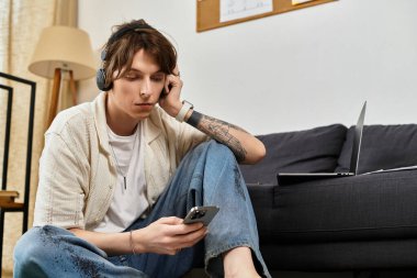 Genç bir öğrenci evde oturup kulaklıkla müzik dinlerken telefonuna odaklanıyor..