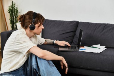 Odaklanmış genç adam, kulaklıklar ve okul malzemeleriyle evde ders çalışıyor..