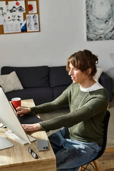 Genç bir adam ahşap bir masada oturuyor, rahat bir ev ortamında bilgisayarın başında ders çalışıyor..