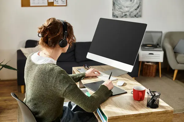 Odaklanmış genç öğrenci rahat bir ofis ortamında masa başında notlar alırken kulaklık takıyor..
