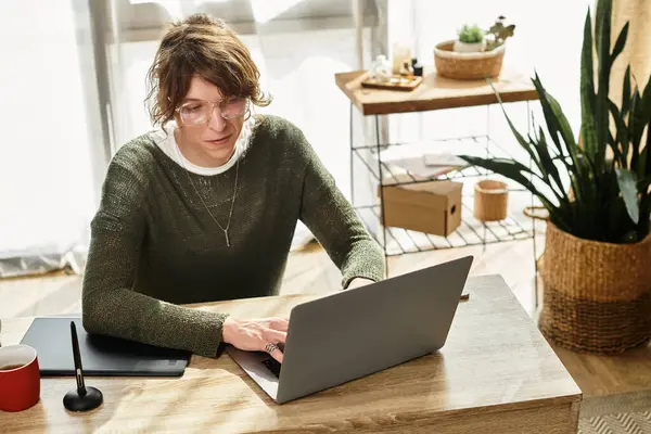 Genç bir adam, parlak ve rahat bir yerde çalışırken bir dizüstü bilgisayar başında oturuyor..