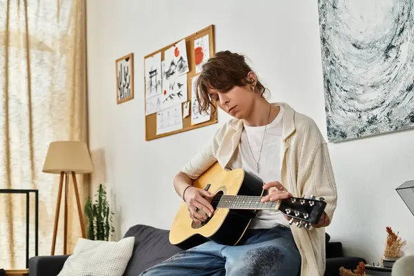 Genç bir adam sıcak, davetkar bir odada gitar çalarak koltukta oturur..