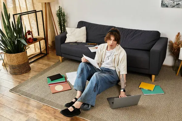 Evde ders kitabı ve verimli bir ortamda dizüstü bilgisayarla çevrili genç bir adam okuyor..