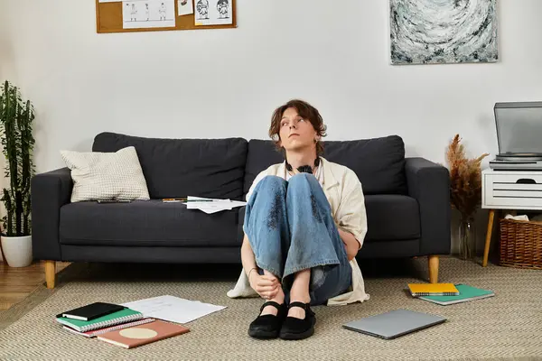 Öğrenci evde yerde oturmuş, etrafı defterlerle çevrili, çalışmalarını derinlemesine düşünüyor..