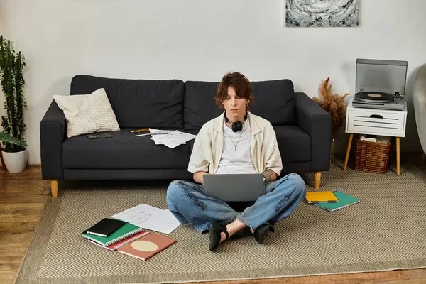 Yerde dizüstü bilgisayarı olan, rahat bir evde kitaplarla çevrili bir adam..