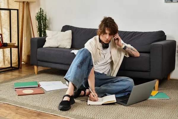 Genç bir adam evde rahat bir şekilde otururken ödevlerini yapar, etrafı çalışma malzemeleriyle çevrilidir..