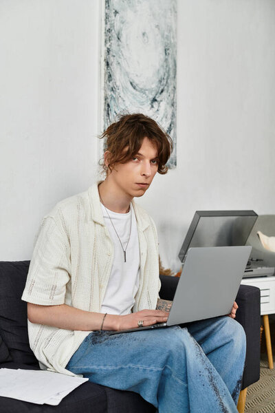 A young student is seated on a cozy couch, deeply engaged in studies on his laptop.