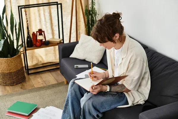 Genç bir adam rahat bir şekilde kanepede oturur, defterine yazarken derinden odaklanır..