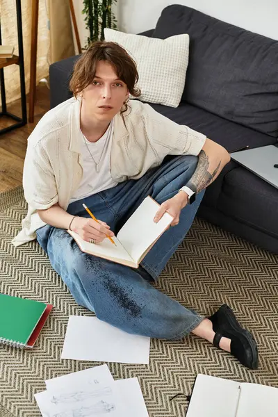 Genç adam, çalışma materyalleriyle çevrili defterine fikirler çiziyor..