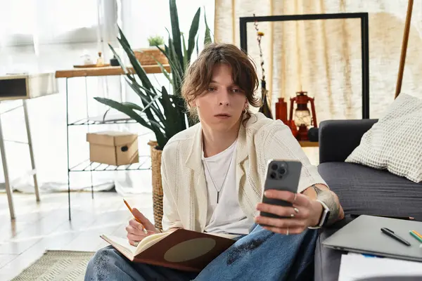 Genç adam rahat bir ev atmosferiyle çevrili telefonunda çalışma materyallerini araştırıyor..