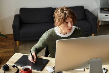 Genç bir adam çalışma masasında yaratıcı işler yapıyor, dijital tablet üzerinde yoğunlaşıyor..
