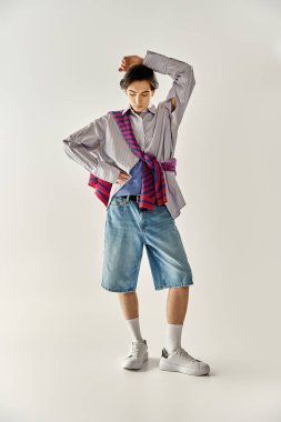 İkili olmayan genç bir kişi, günlük şortları ve katmanlı üst katmanları olan modaya uygun bir kıyafet sergiliyor..