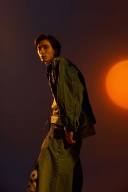 İkili olmayan bir genç modern modada canlı bir günbatımına karşı güvenle poz verir..