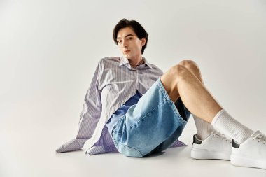 İkili olmayan genç bir kişi yerde şık bir şekilde poz verir ve benzersiz kimliğini benimser..