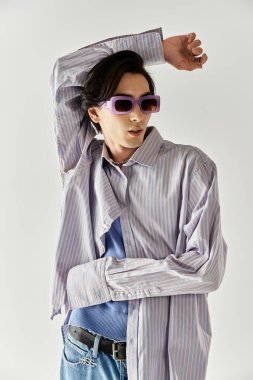 İkili olmayan genç birey, minimalist bir arkaplana karşı şık giyinerek güven içinde poz veriyor..