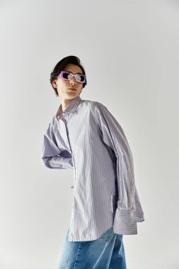 İkili olmayan genç bir kişi, tarafsız bir arkaplana karşı kendine güvenen moda tarzını sergiliyor.