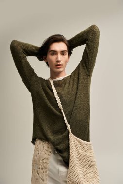 Modayı takip etmeyen bir kişi, yumuşak bir arkaplan karşısında şık giyinerek güven içinde poz verir..