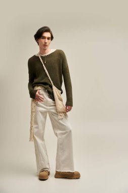 İkili olmayan genç bir kişi kendine güvenerek duruyor, yetenekli ve yaratıcı bir kıyafet sergiliyor..