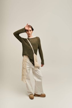 Şık, genç, ikili olmayan bir kişi, yumuşak, nötr bir arkaplana karşı güvenle poz verir..