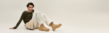 İkili olmayan genç bir kişi, minimalist bir alanda, pankartta canlı bir moda sergiliyor.