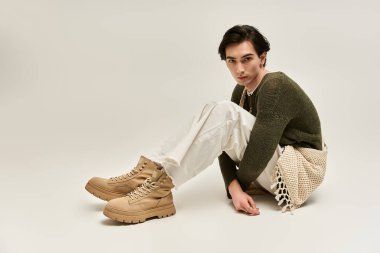 İkili olmayan genç bir kişi zarif bir şekilde otururken şık bir kıyafet sergiliyor..