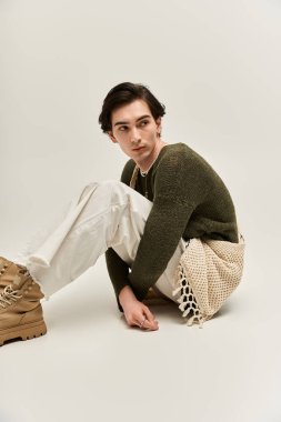 İkili olmayan bir kişi şık ve minimalist bir ortamda otururken moda sergiliyor.