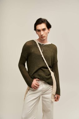 İkili olmayan genç bir insan, sakin bir stüdyo içinde kendine güvenen şık bir kıyafetin içinde duruyor..