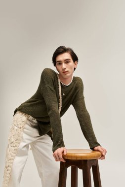 İkili olmayan genç bir insan, kendine güvenen bir şekilde ahşap bir tabureye poz verir ve kendi eşsiz tarzını ifade eder..