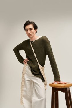 Genç, modaya uygun, ikilik olmayan bir kişi duruşuyla duruyor ve modaya uygun bir kıyafet sergiliyor..