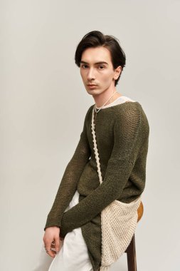 Tarz sahibi, ikili olmayan bir birey, modern moda eğilimlerini somutlaştıran şık bir kıyafetin içinde güven içinde poz verir..