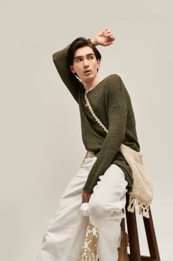 İkili olmayan genç bir birey, bir taburede şık bir şekilde poz verir, kimliğini ve modasını ifade eder..