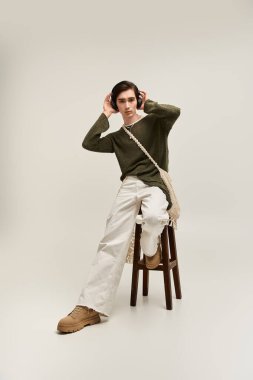 Genç, modaya uygun olmayan bir kişi, kendine güvenen bir şekilde bir taburede poz verir ve benzersiz tarzını sergiler..