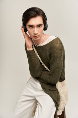 İkili olmayan kişi, minimal arka planda kulaklıkla şık bir moda sergiliyor.