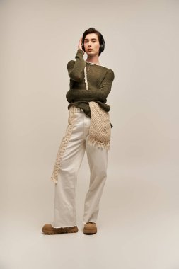 Şık giyinmiş, ikiyüzlü olmayan genç bir insan düşünceli bir şekilde ışık dolu bir stüdyoda poz verir..