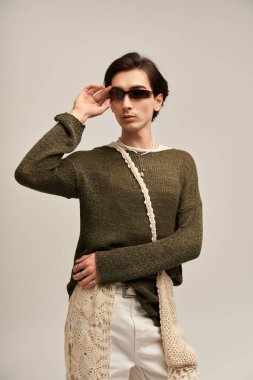 İkili olmayan kendine güvenen bir genç, minimalist bir stüdyoda eşsiz bir süveter ve pantolon giyer..