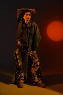 Canlı bir arkaplan karşısında kendine güvenle poz veren bu kişi, kendine has bir stil ve kimliğe sahiptir..