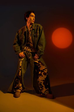 İkili olmayan genç bir birey, eşsiz modalarını renkli bir arkaplana karşı sergiliyor.