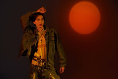 Şık, genç, ikili olmayan bir birey, büyük turuncu bir güneşin önünde moda sergiliyor..