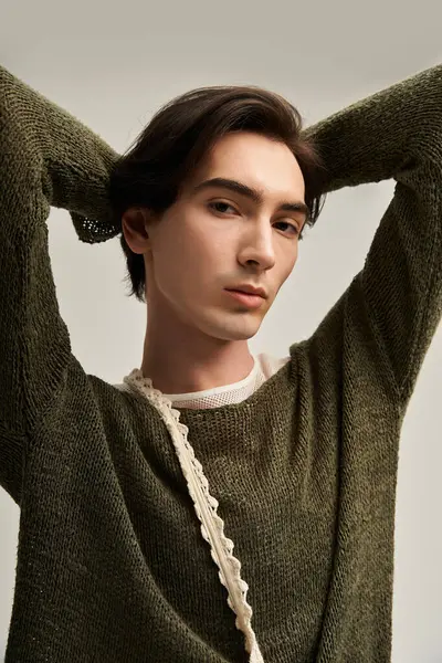 İkili olmayan bir genç, minimalist bir stüdyoda kendine güvenen şık örgü bir süveter modeller..