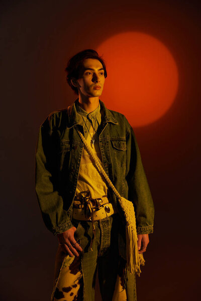 Стильный молодой небинарный человек уверенно стоит, освещенный ярким закатом.