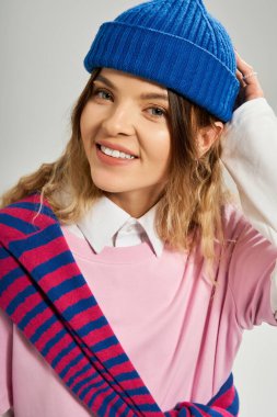 Mavi bereli güzel bir genç bayan, modaya uygun bir stüdyo ortamında kendine güvenerek gülümsüyor..