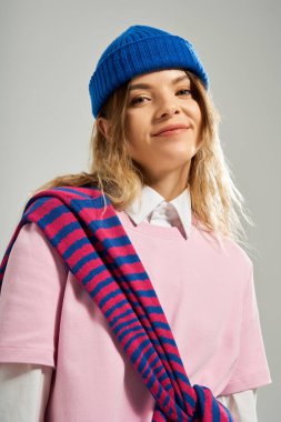 Genç bir kadın, modaya uygun bir kıyafet ve stüdyoda mavi bereyle poz veriyor..