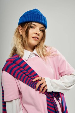 Genç bir kadın, stüdyo ortamında mavi bereli modaya uygun kıyafetini sergiliyor.