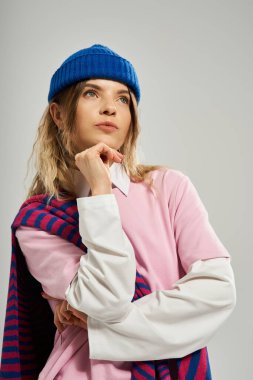 Genç bir kadın zarif bir şekilde poz verir. Stüdyoda parlak mavi bir bere takar..