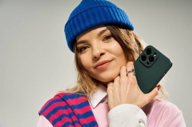 Genç bir kadın moda anlayışını akıllı telefonuyla bir stüdyo arkaplanına gösteriyor..